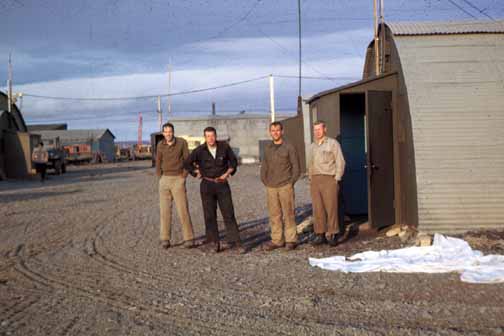 photo, four men posing outside a quansit hut