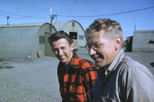 photo, two men standing among Quonset huts
