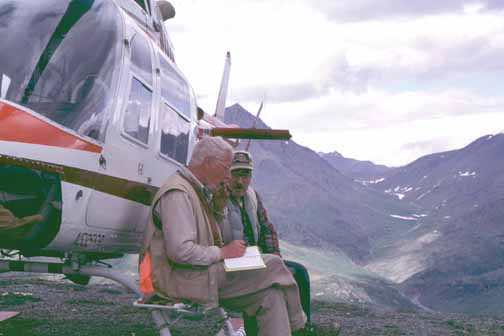 photo, two men sitting on the step of a parked helicopter