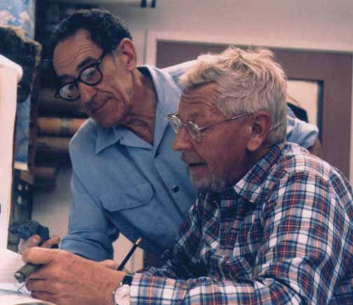 photo, closeup of two mein in an office looking at a rock.  Bill has a cigar in his hand as usual